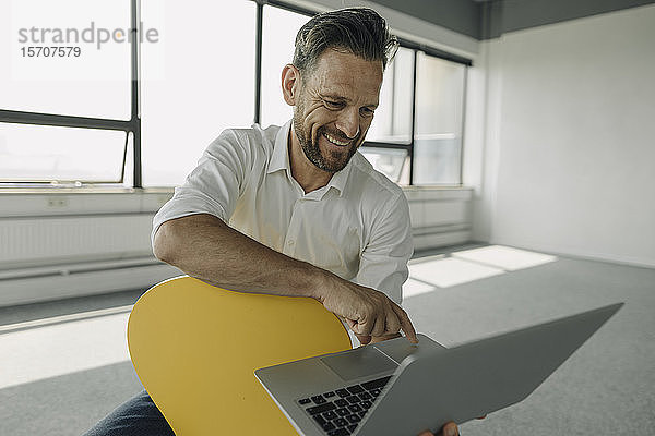 Lächelnder reifer Geschäftsmann mit Laptop im leeren Büro