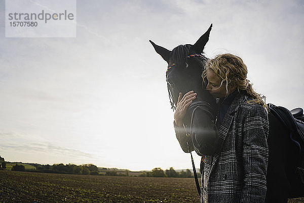 Liebevolle junge Frau mit Pferd auf einem Feld auf dem Land bei Sonnenuntergang