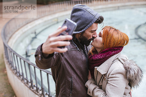 Küssendes Paar  das sich mit dem Smartphone selbstständig macht
