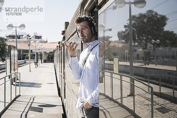 Junger Mann mit Kopfhörer und Smartphone in der Zugtür
