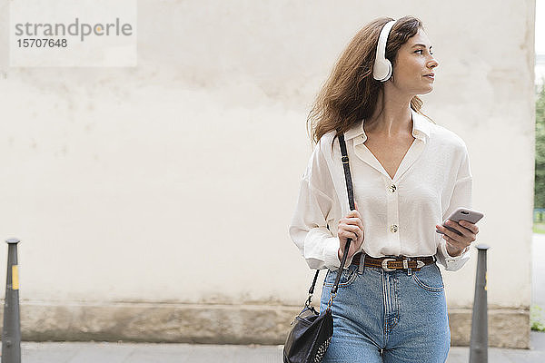Junge Frau mit Smartphone und Kopfhörern in der Stadt unterwegs