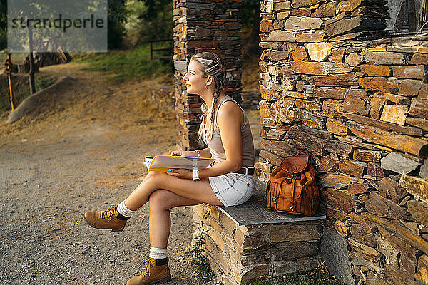 Frau mit Ordner sitzt an einem Steinhaus auf dem Land