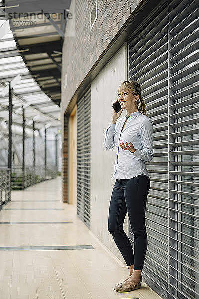 Lächelnde junge Geschäftsfrau am Telefon in einem modernen Bürogebäude