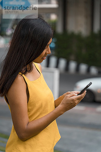 Modische Frau in gelb gekleidet schaut auf Smartphone