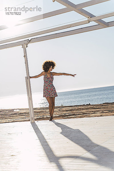 Junge Frau im Sommerkleid genießt das Sonnenlicht auf einer Terrasse am Strand