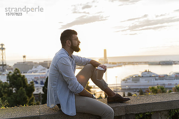 Mann sitzt auf einer Mauer auf einem Aussichtspunkt über der Stadt mit Blick auf den Hafen  Barcelona  Spanien