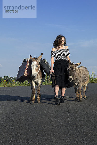 Junge Frau auf Landstraße mit Gepäck tragenden Eseln