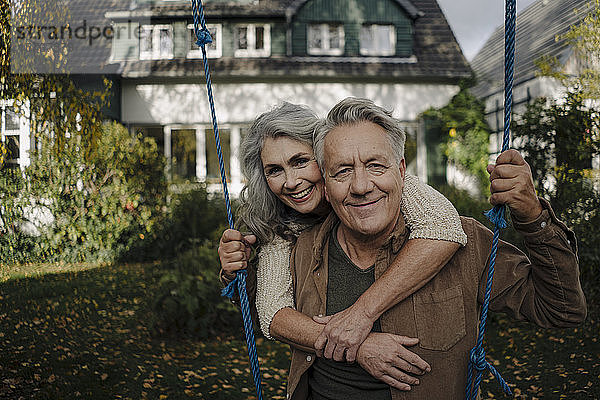 Porträt einer glücklichen Frau  die einen älteren Mann auf einer Schaukel im Garten umarmt