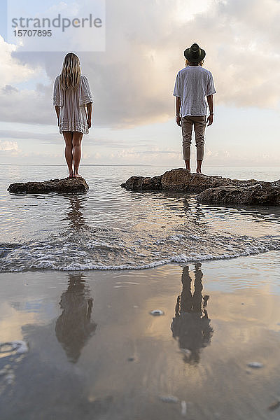 Rückenansicht eines jungen Paares  das auf Felsen vor dem Meer steht  Ibiza  Balearen  Spanien