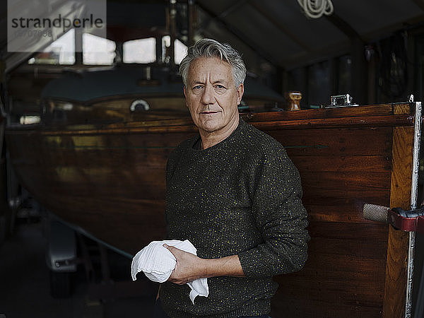 Bildnis eines älteren Mannes mit Tuch am Holzboot in einem Bootshaus
