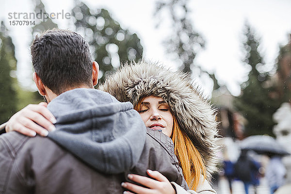 Porträt einer jungen Frau mit geschlossenen Augen  die ihren Freund im Freien umarmt