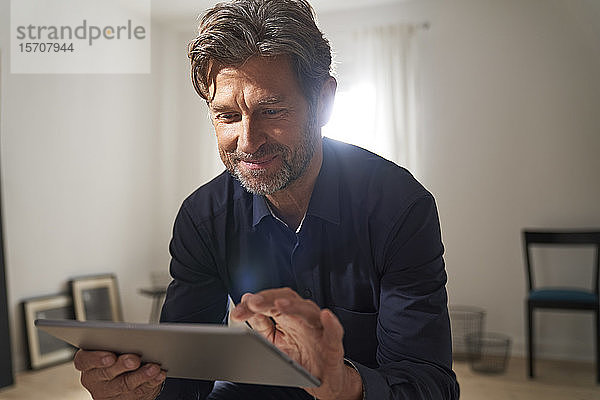 Porträt eines lächelnden  reifen Mannes  der zu Hause ein digitales Tablet benutzt