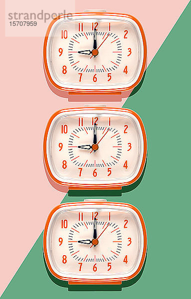 3D-Illustration  Reihe von orangefarbenen Weckern bei neun Uhr auf rosa und mintgrünem Hintergrund
