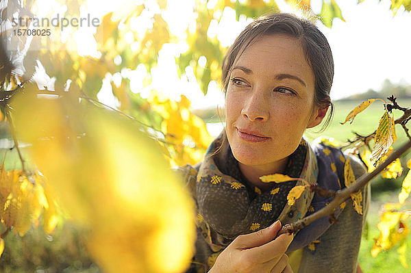 Porträt einer Frau an Zweigen mit Herbstlaub  die in die Kamera schaut