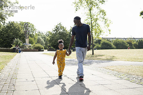 Vater und Tochter gehen Hand in Hand auf einem Weg in einem Park