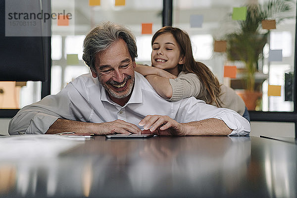 Glücklicher leitender Geschäftsmann und Mädchen schauen auf Tablett im Büro