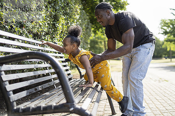 Vater hilft Tochter beim Klettern auf eine Parkbank