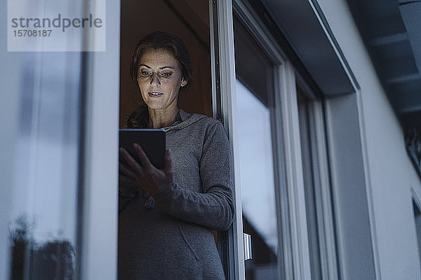 Frau steht in Balkontür und benutzt digitales Tablett