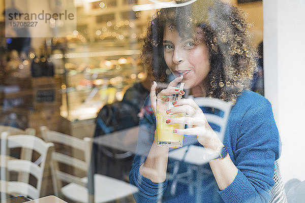 Porträt einer Frau  die in einem Cafe hinter einer Fensterscheibe einen Smoothie trinkt
