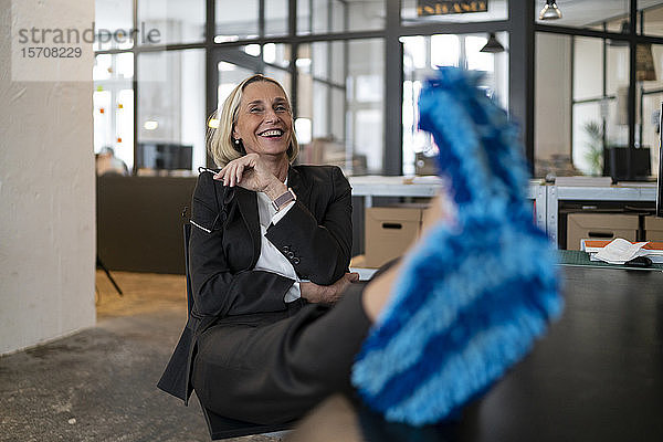 Lachende reife Geschäftsfrau mit Füßen auf dem Schreibtisch und Reinigungsschuhen im Büro
