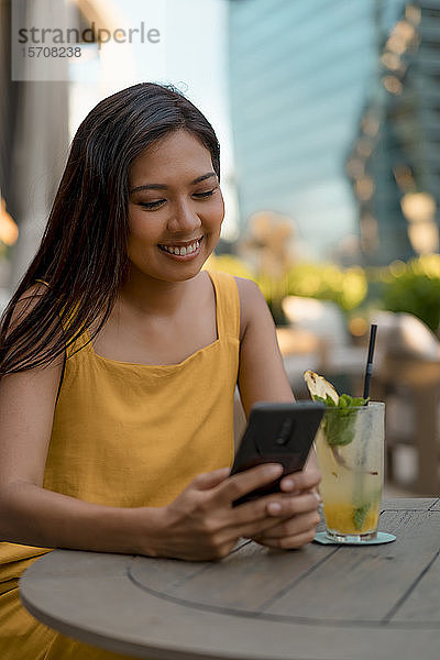Porträt einer lächelnden Frau  die in einem Cafe sitzt und auf ihr Handy schaut
