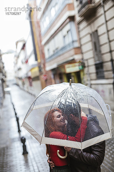 Verliebtes Paar küsst sich unter einem transparenten Schirm in der Stadt