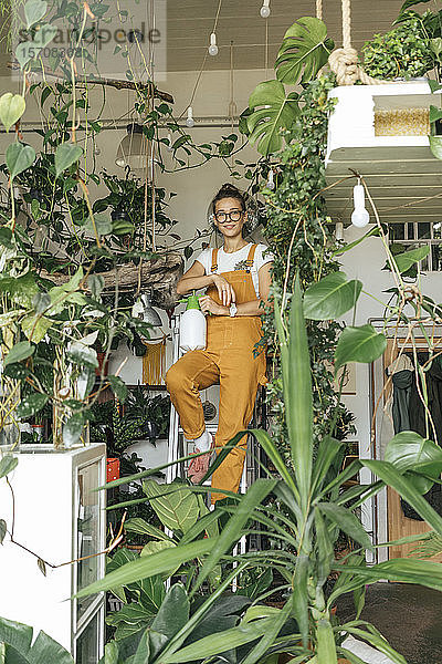 Porträt einer jungen Frau  die auf einer Leiter in einem kleinen Gartenbaubetrieb steht