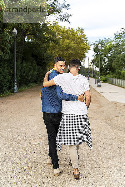 Rückenansicht eines glücklichen schwulen Paares  das Arm in Arm in einem Park geht  Barcelona  Spanien