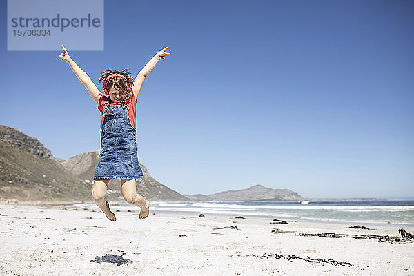 Mädchen hört Musik mit Kopfhörern am Strand  springt in die Luft  Kapstadt  Western Cape  Südafrika