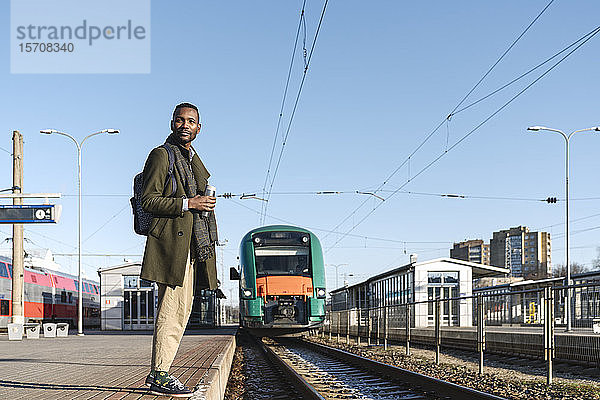 Porträt eines stilvollen Mannes mit wiederverwendbarem Becher  der auf den Zug wartet