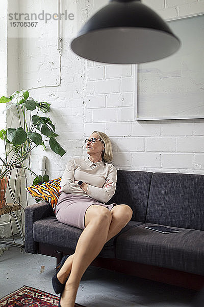 Reife Geschäftsfrau sitzt mit geschlossenen Augen auf der Couch in der Bürolounge