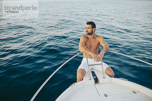Junger Mann sitzt am Bug eines Bootes und beobachtet das Meer
