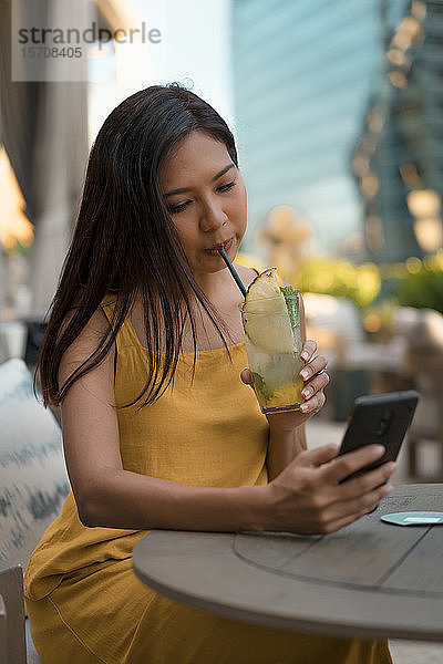 Porträt einer Frau  die mit einem Getränk in einem Cafe sitzt und auf ihr Handy schaut