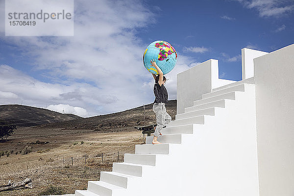 Kleines Mädchen auf weißer Treppe  das einen aufblasbaren Globus trägt