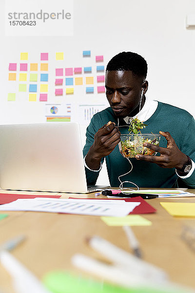 Mann mit Laptop sitzt am Schreibtisch im Büro und macht Mittagspause