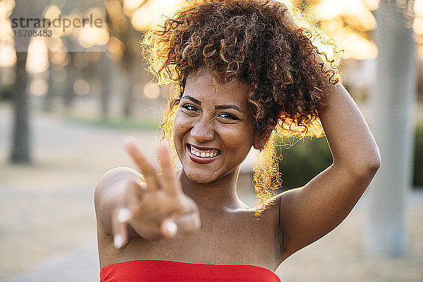 Junge glückliche Frau drückt V-Geste mit den Fingern aus
