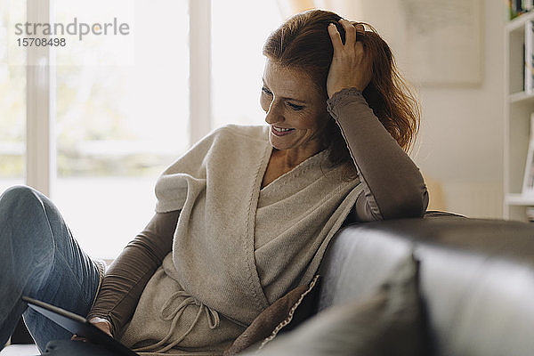 Lächelnde Frau sitzt auf dem Sofa und benutzt ein digitales Tablett