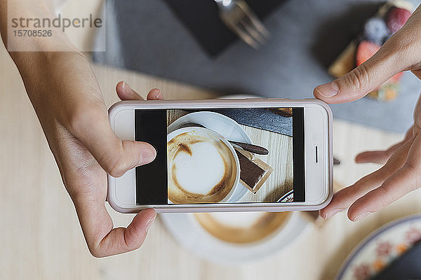 Draufsicht einer Frau in einem Cafe  die ein Handyfoto von Cappuccino macht