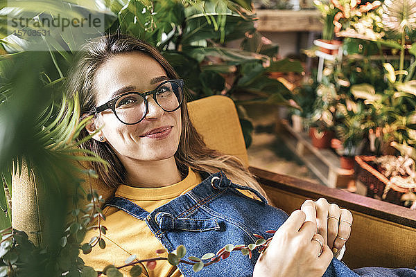 Porträt einer lächelnden jungen Frau im Sessel sitzend  umgeben von Pflanzen