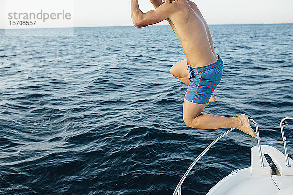 Junger Mann springt aus einem Boot ins Meer