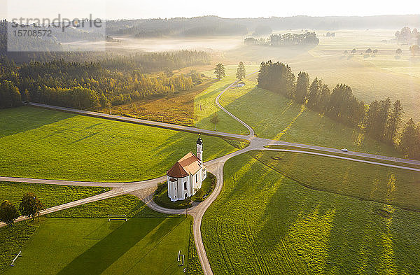 Deutschland  Bayern  Dietramszell  Luftaufnahme der ländlichen Felder und der Kirche St. Leonhard bei nebliger Morgendämmerung
