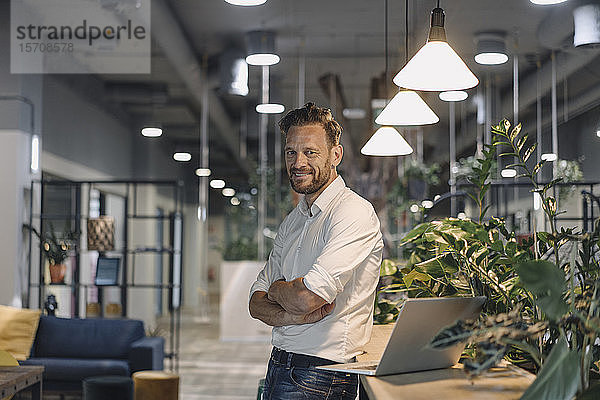 Porträt eines lächelnden reifen Geschäftsmannes mit Laptop in moderner Büro-Lounge