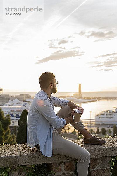 Mann sitzt auf einer Mauer auf einem Aussichtspunkt über der Stadt mit Blick auf den Hafen  Barcelona  Spanien