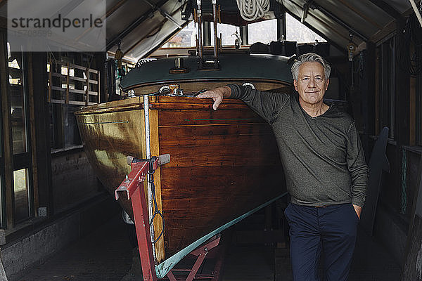 Porträt eines stolzen älteren Mannes auf einem Holzboot in einem Bootshaus