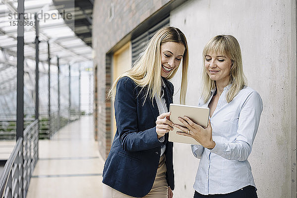 Zwei glückliche junge Geschäftsfrauen mit Tablett in modernem Bürogebäude