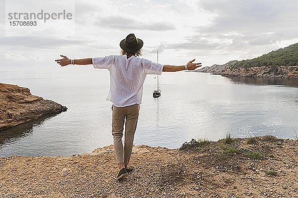 Rückenansicht eines glücklichen jungen Mannes vor dem Meer  Ibiza  Balearen  Spanien