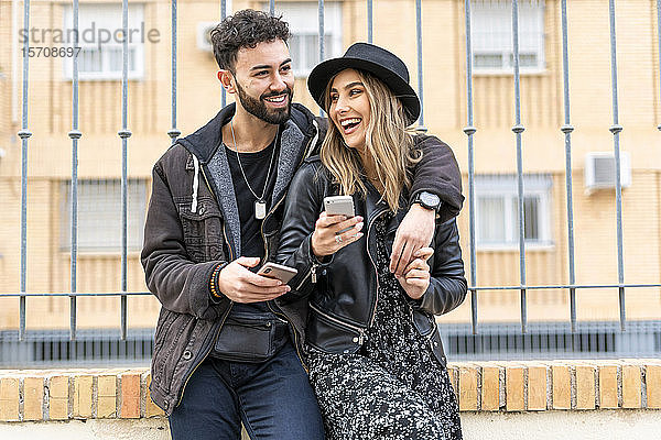 Porträt eines lachenden jungen Paares mit ihren Mobiltelefonen in der Stadt