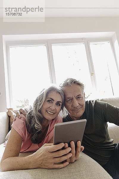 Porträt eines glücklichen älteren Paares  das sich zu Hause auf der Couch mit Tablette entspannt