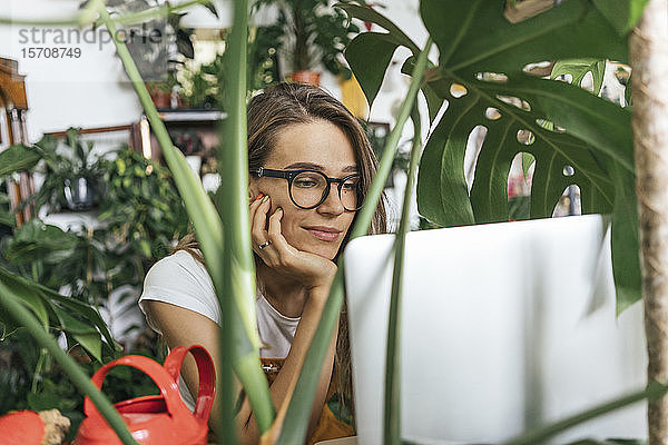 Junge Frau benutzt Laptop inmitten von Pflanzen
