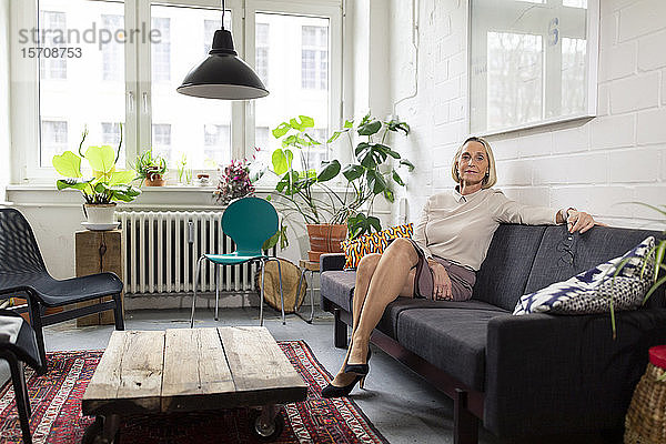 Reife Geschäftsfrau sitzt auf Couch in Büro-Lounge